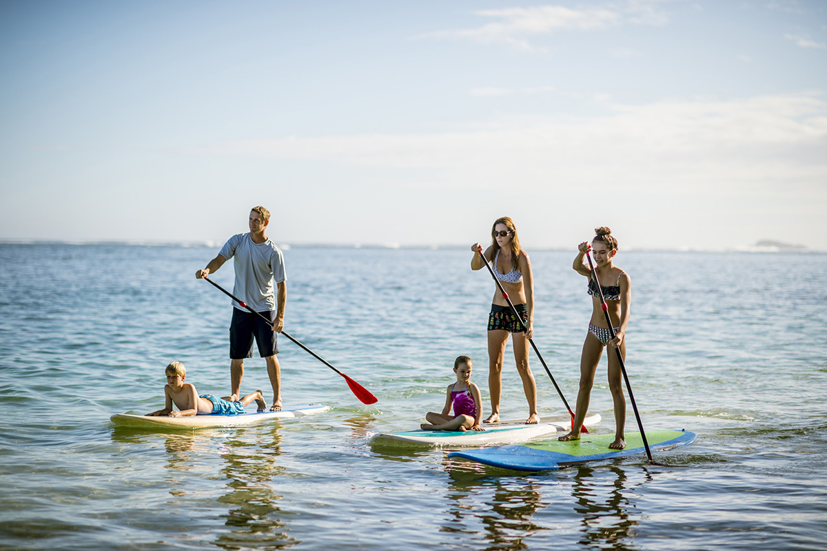 Family in Hawaii's tropical climate enjoying their vacation on stand up paddleboards (SUP) in the sea.