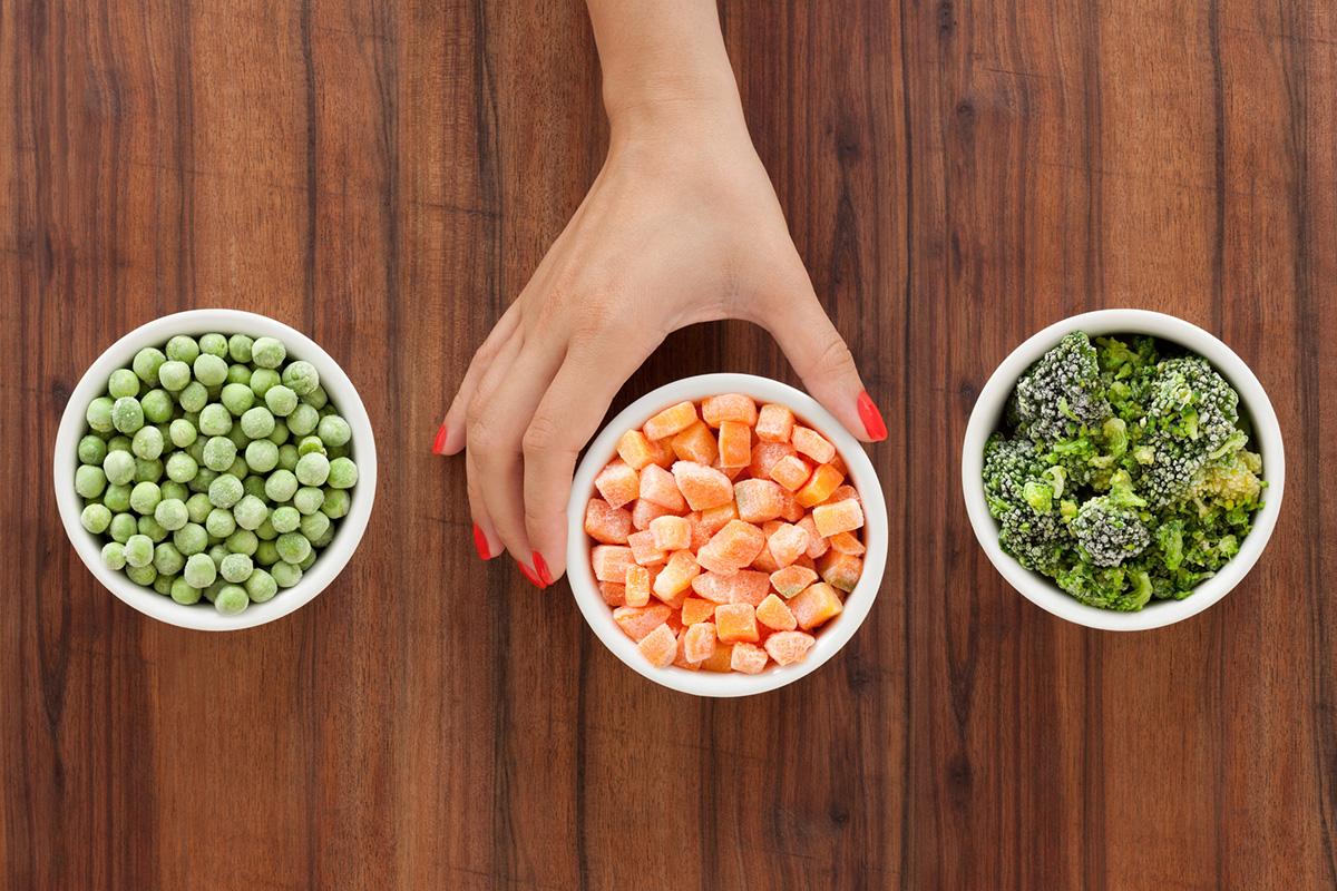 Three bowls with varieties of frozen vegetables and woman's hand holding the middle one